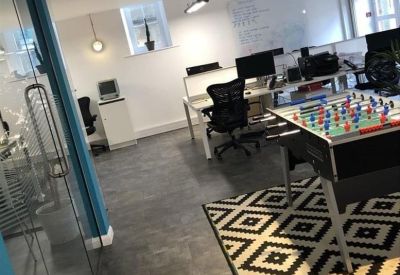Open-plan office area with a foosball table, patterned rug, and multiple workstations.