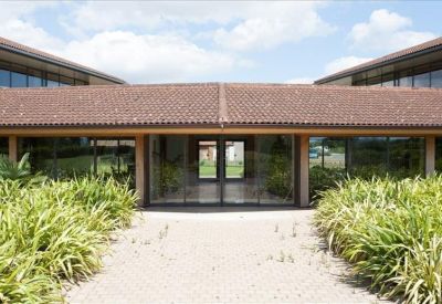 Glass-fronted building entrance with a tiled walkway and flanking green plants.