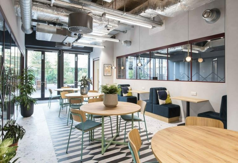 Bright communal lounge at 2 Whitechapel Road featuring round wooden tables and navy blue booths.