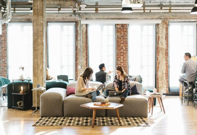 Spacious communal lounge at 8 Devonshire Square, London with brick walls and comfortable grey sofas.