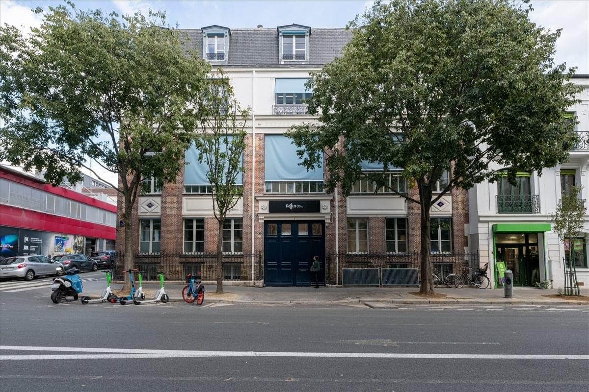 Exterior view of the classic stone facade at 64 Avenue Parmentier, Paris with large windows and trees.