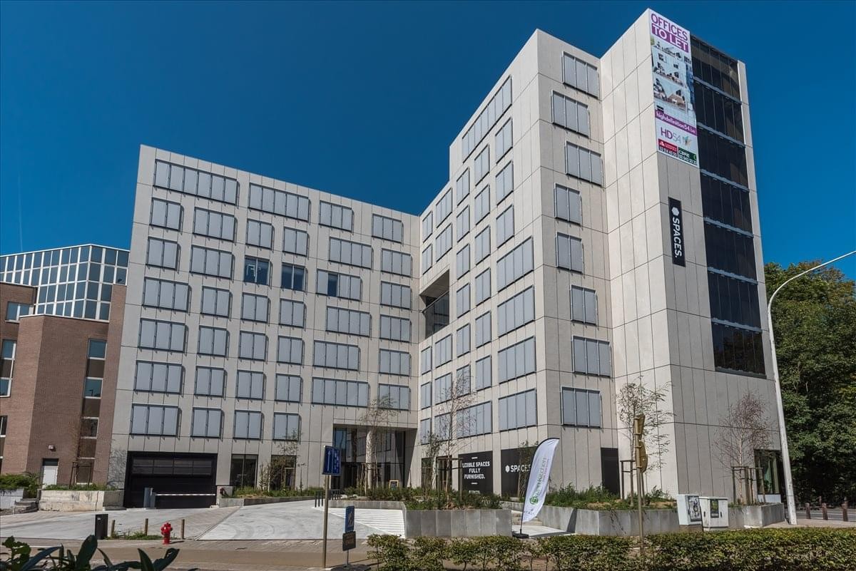 Modern exterior facade of Avenue Herrmann Debroux 54 with large windows and a clear blue sky.