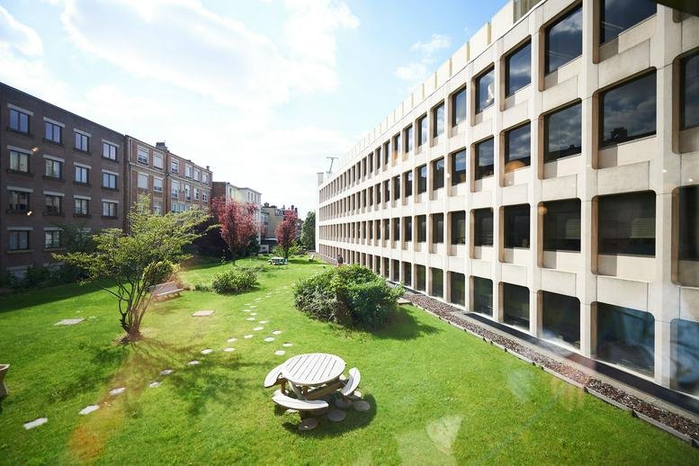 Exterior view of the white grid facade at Avenue Louise 235 with a green lawn and patio seating.