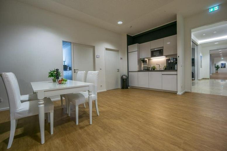 Modern white communal kitchen and dining area with light wood flooring.