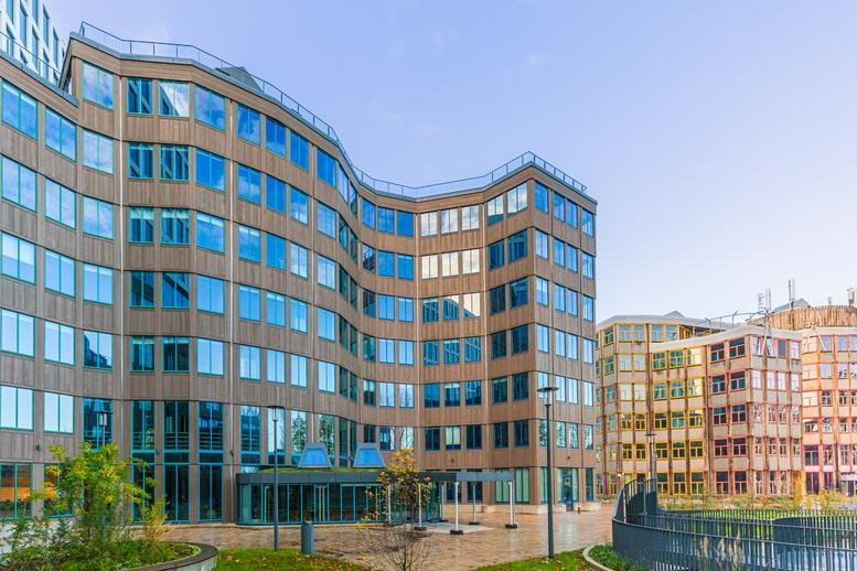 Modern office building with a curved glass facade and paved courtyard.