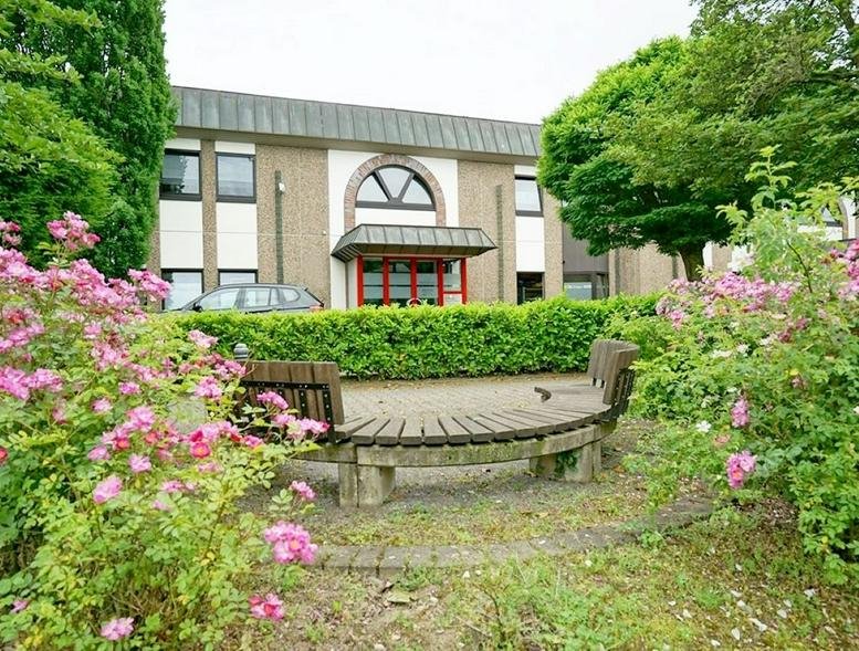 Exterior view of the office building at Kimplerstraße 278-296 with a curved wooden bench and pink flowers.