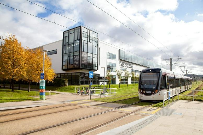 Exterior of the modern white and glass Pure Offices building with a tram passing by.