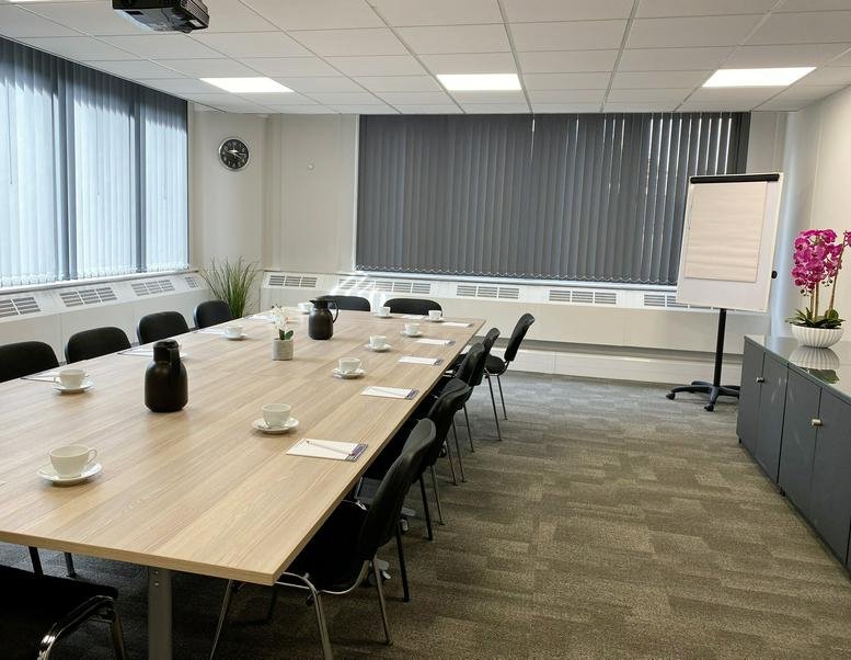 Spacious boardroom with a long light-wood table, multiple chairs, and a flipchart.