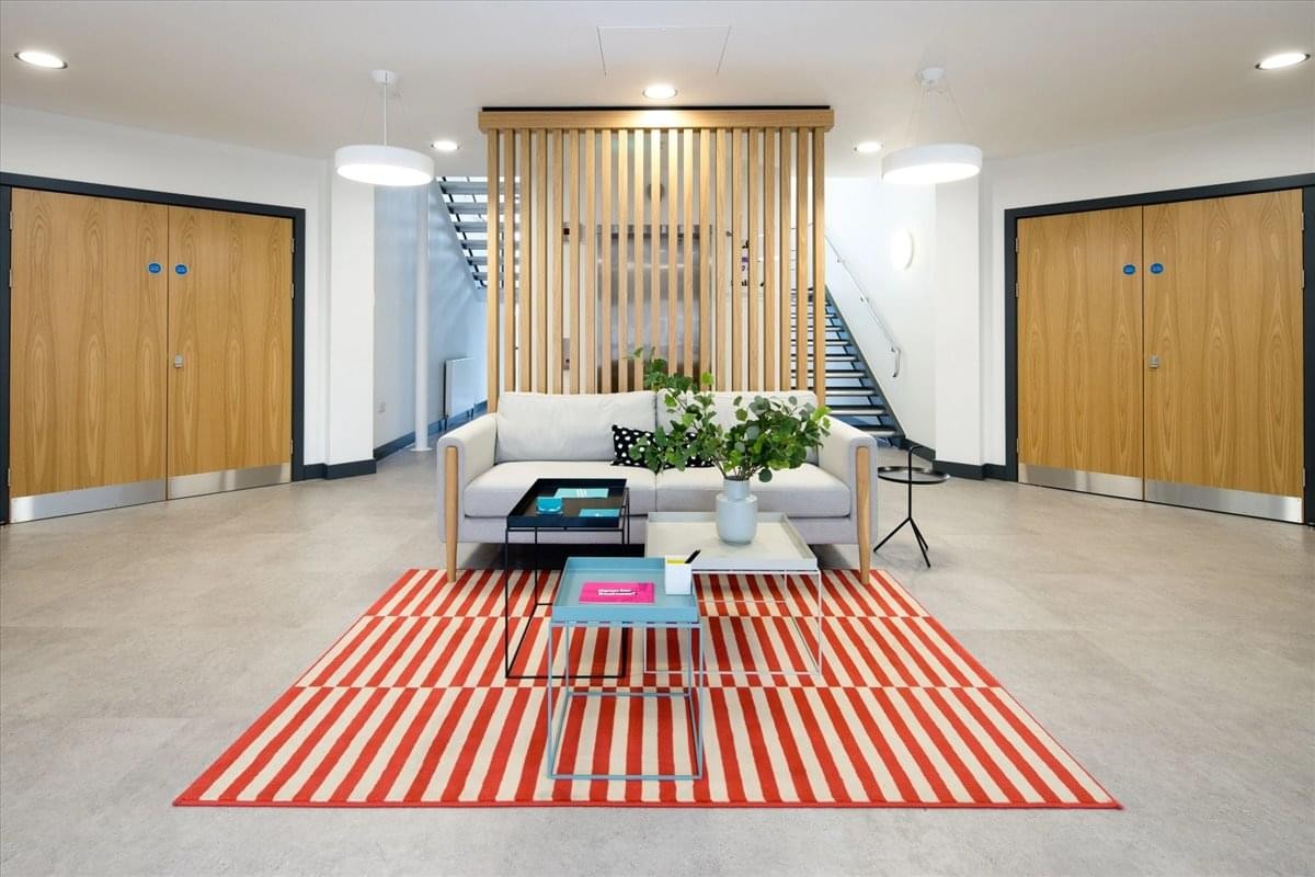 Spacious reception at Equinox South with a neutral sofa, red striped rug, and light wood screen.