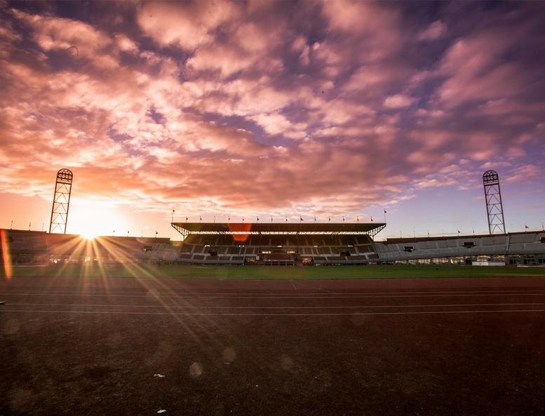 Exterior view of the historic Olympisch Stadion 24-28 under a vibrant purple and orange sunset.