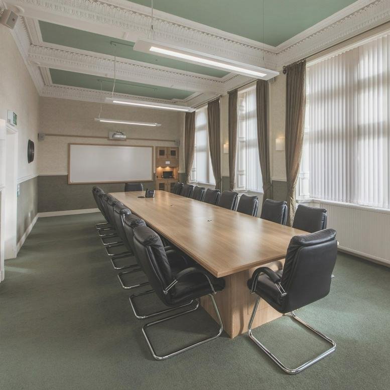 Boardroom with a long wooden table, black leather chairs, and tall windows.