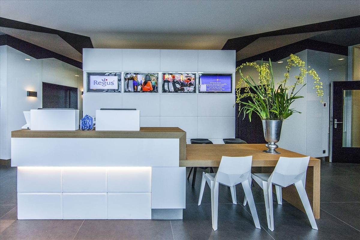 Modern reception area with a white desk, wooden accents, and vibrant green plants.