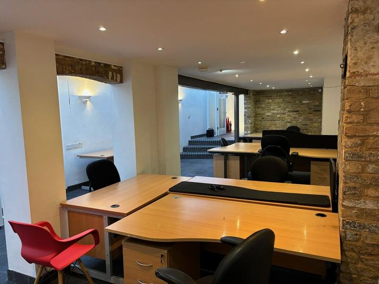 Open-plan office space featuring wooden desks, black chairs, and a red accent chair.