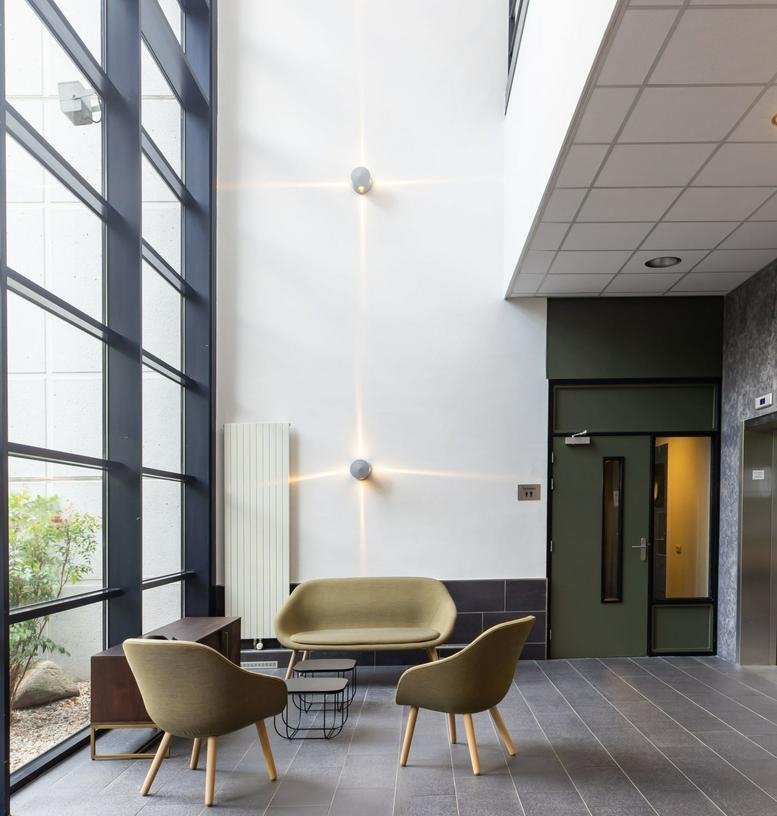 High-ceiling reception lobby at Overschiestraat 59 with modern olive-green seating and tall glass windows.