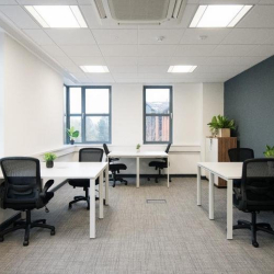 Bright internal office space featuring multiple workstations, large windows, and grey carpeting.
