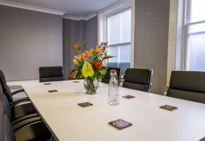 Bright boardroom with white table, black leather chairs, and a floral centerpiece.