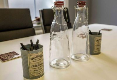 Close-up of vintage-style water bottles and pen holders on a white meeting table.