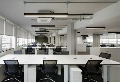 Bright open-plan office with white desks, black mesh chairs, and linear pendant lighting.