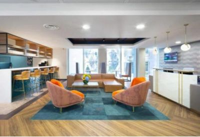 Modern reception lobby with orange armchairs, a teal rug, and a sleek front desk.