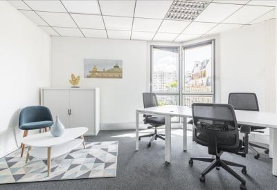 Bright corner office with white desks, mesh chairs, and a geometric rug.