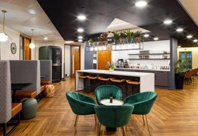 Open-plan breakout space featuring green velvet armchairs, private booths, and a coffee station.