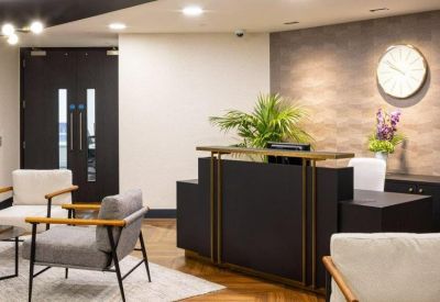 Close-up of a modern dark wood reception desk with a backlit wall clock and indoor greenery.