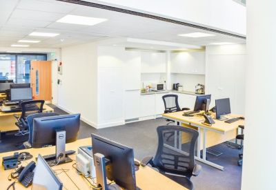 Modern office interior featuring workstations and a sleek white kitchen area in the background.