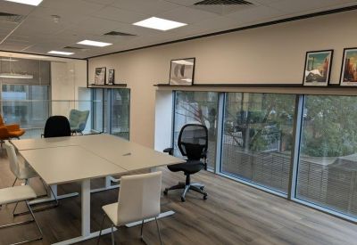 Bright meeting room with large windows, white tables, and ergonomic mesh chairs.