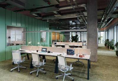 Open-plan coworking area with long white desks, ergonomic seating, and exposed industrial ceilings.
