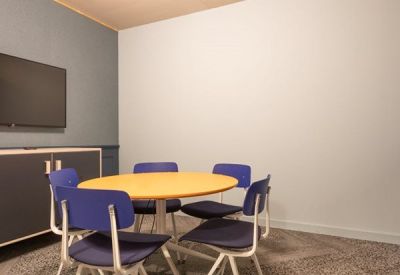 Private office space with a yellow round table and a wall-mounted flat screen.