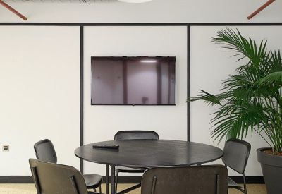 Meeting room with a round black table, dark chairs, and a large wall-mounted monitor.