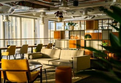 Sunny meeting area with a cream sofa, yellow armchair, and wood-framed room dividers.