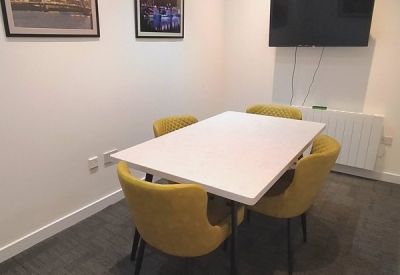 Private four-person meeting room with yellow chairs, a white table, and wall-mounted monitor.