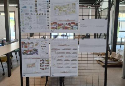 Black wire mesh display stand with architectural drawings and project sketches in a bright workspace.