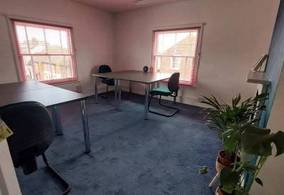 Open-plan office space with multiple desks and blue carpeting.