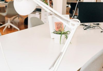 Bright office space featuring white desks, adjustable lamps, and grey chairs.
