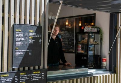 Outdoor coffee kiosk serving refreshments near a shaded seating area.