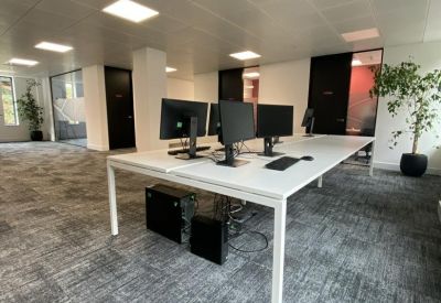 Open-plan office with white desks, black monitors, and grey carpeting.