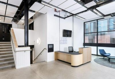 Modern reception desk with light wood paneling and a blue lounge chair in a bright lobby.