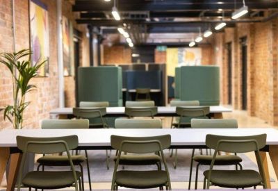 Open-plan office with rows of green chairs at white desks set against an industrial brick backdrop.