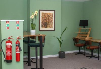 Green-walled coworking corner with high-top seating and a dedicated workstation.