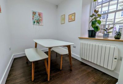 Bright dining area with a white table, wooden benches, and large window with plants.