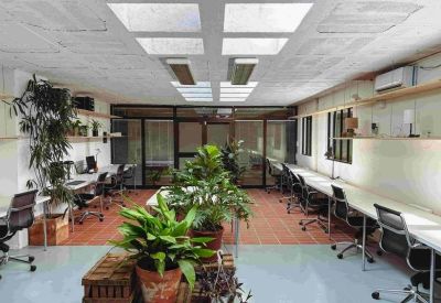 Open office area with red tiled flooring, white desks, and several large leafy plants.
