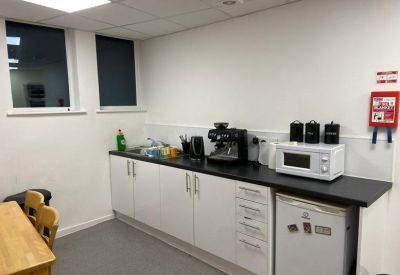 A modern kitchen and breakout area with white cabinetry and a coffee machine.