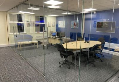 A glass-partitioned meeting room and private office suite with grey carpet tiling.