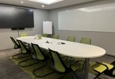 Professional boardroom with an oval white table, green chairs, and a large wall-mounted monitor.