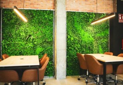 Twin communal work tables set against vibrant vertical plant walls and warm brick accents.