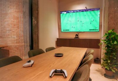 Private meeting room featuring a wooden table, large screen showing a game, and game controllers.
