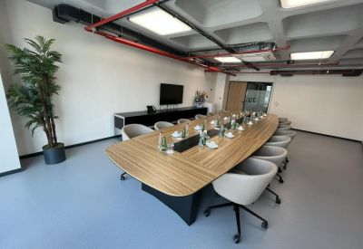Bright boardroom featuring a light wood table, grey chairs, and exposed ceiling details.