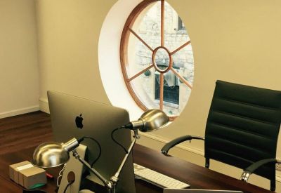 Close-up of a desk with an iMac and adjustable lamps by a unique circular wagon-wheel window.